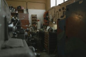 A blacksmith working meticulously with tools in a dimly lit workshop with various equipment around.
